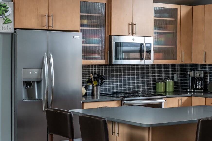Kitchen with black mosaic backsplash, dark refrigerator, and glass front upper cabinets